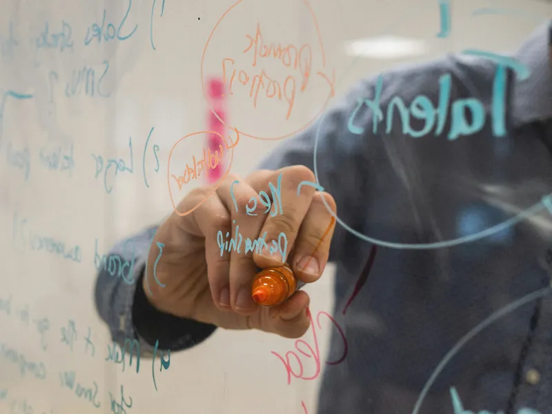 Person writing on glass whiteboard with diagrams